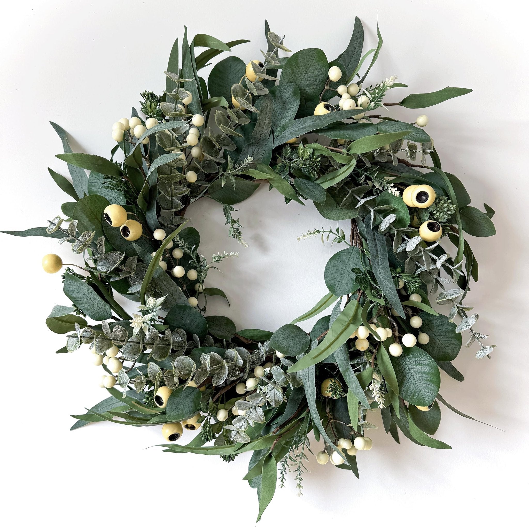 Artificial olive and eucalyptus wreath with white berries and yellow accents on a white background
