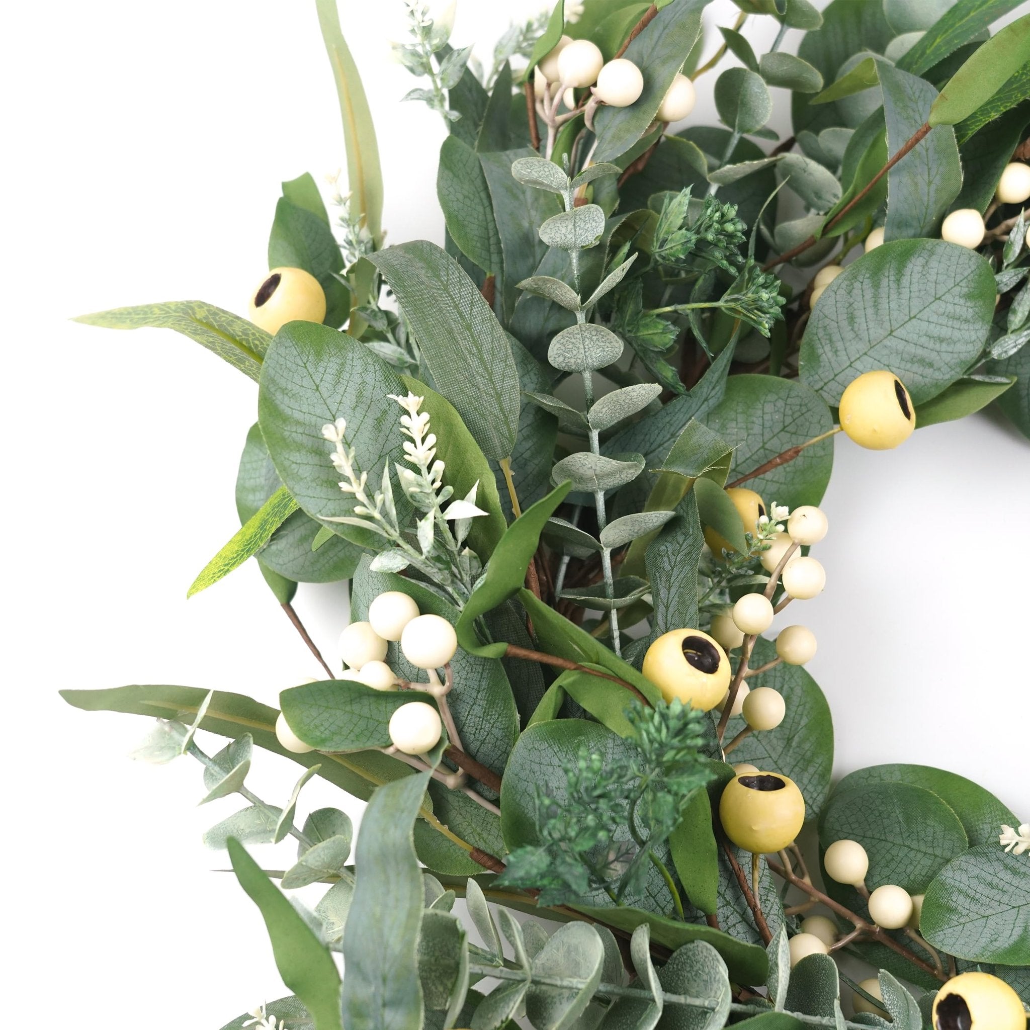 Close-up of an artificial olive and eucalyptus wreath with white berries and yellow accents on a white background.