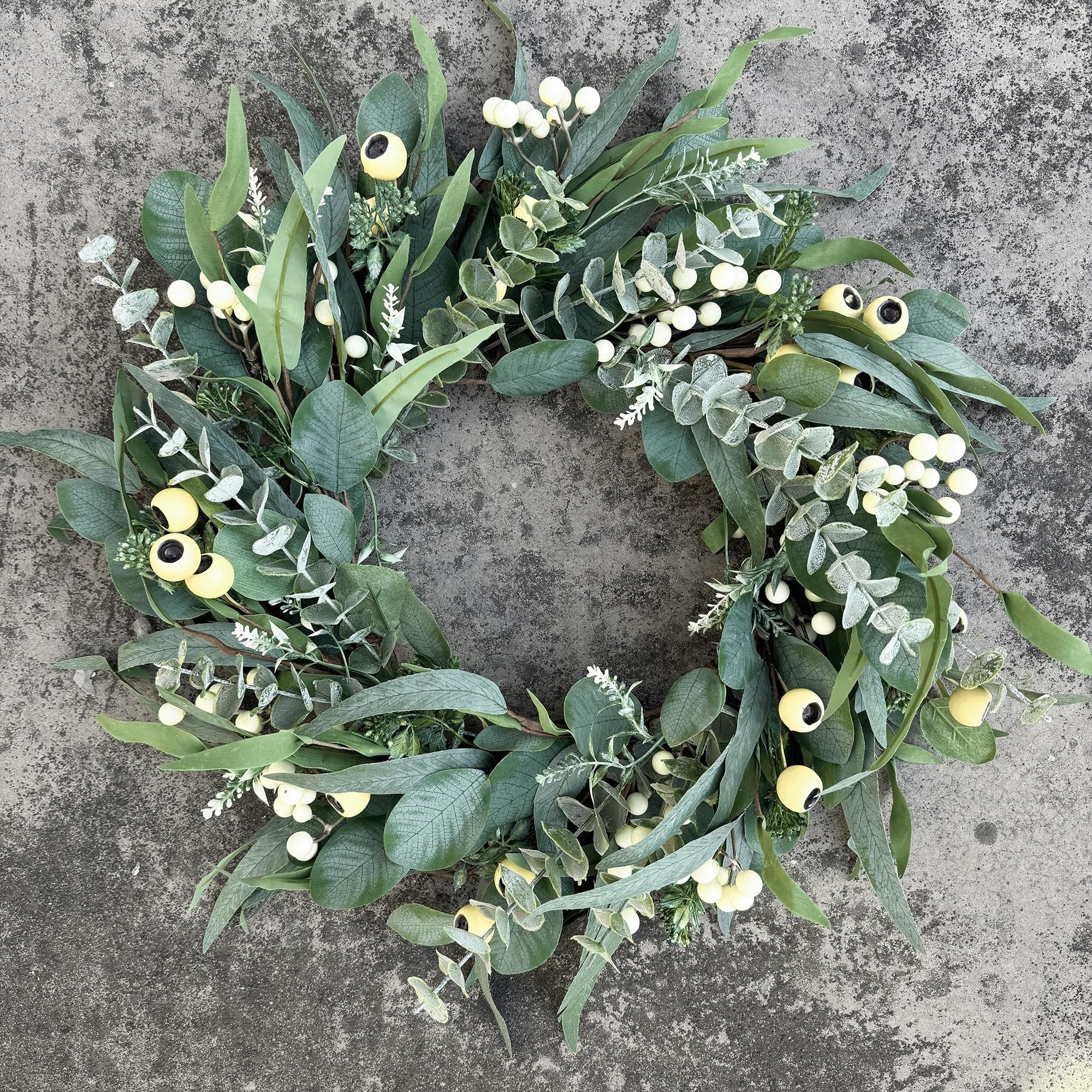 Artificial olive and eucalyptus wreath with white berries and yellow accents on a textured gray surface