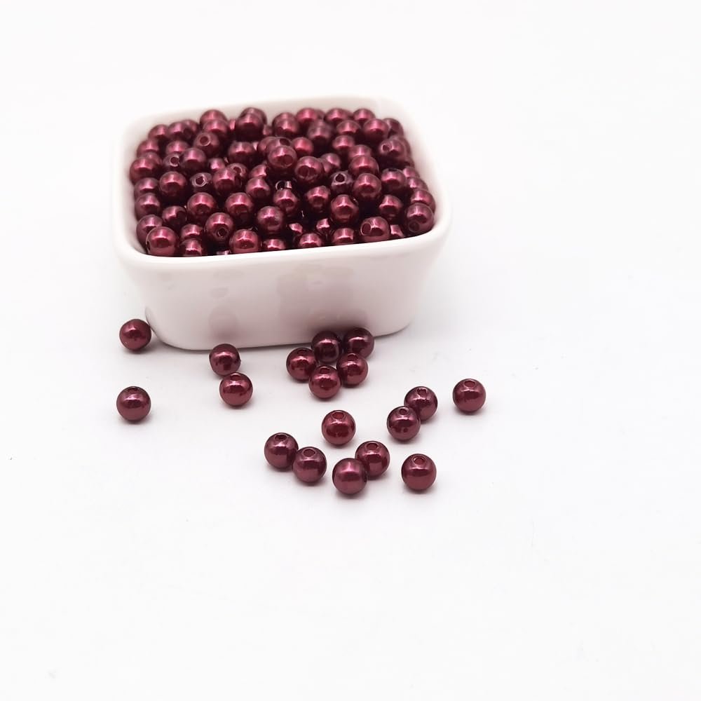 Burgundy plastic pearl spacer beads spilling from a white square bowl onto a white surface.
