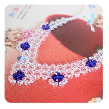 Close-up of a clear faceted bicone bead necklace with blue star accents, laid on a textured red surface.