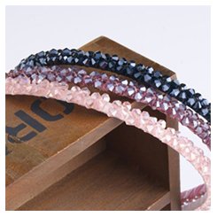 Three beaded headbands in pink, purple, and black, resting on a wooden surface.