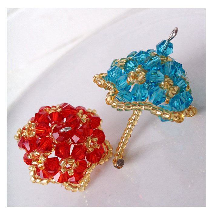 Two beaded charms, one red and one blue umbrella shape, on a white surface.