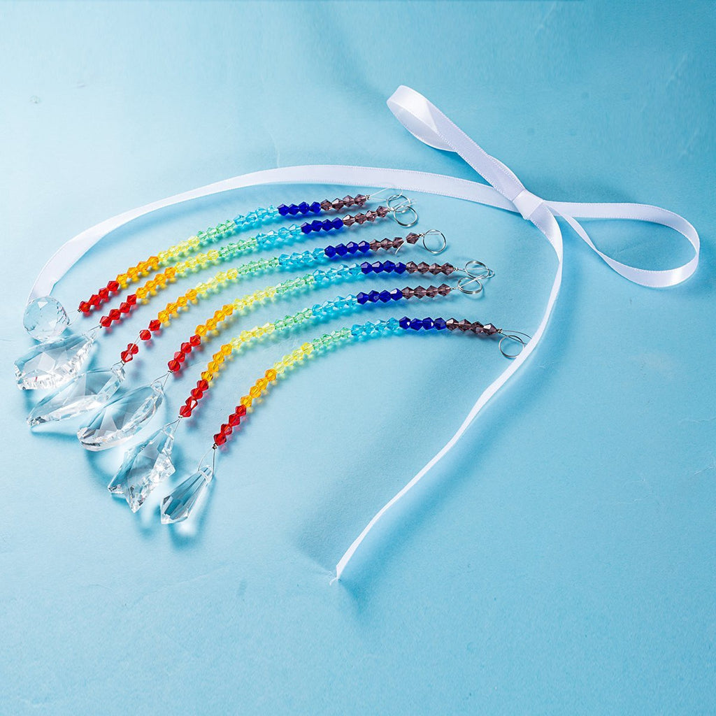 Rainbow crystal suncatcher strands with faceted glass pendants and a white ribbon tie on a blue background