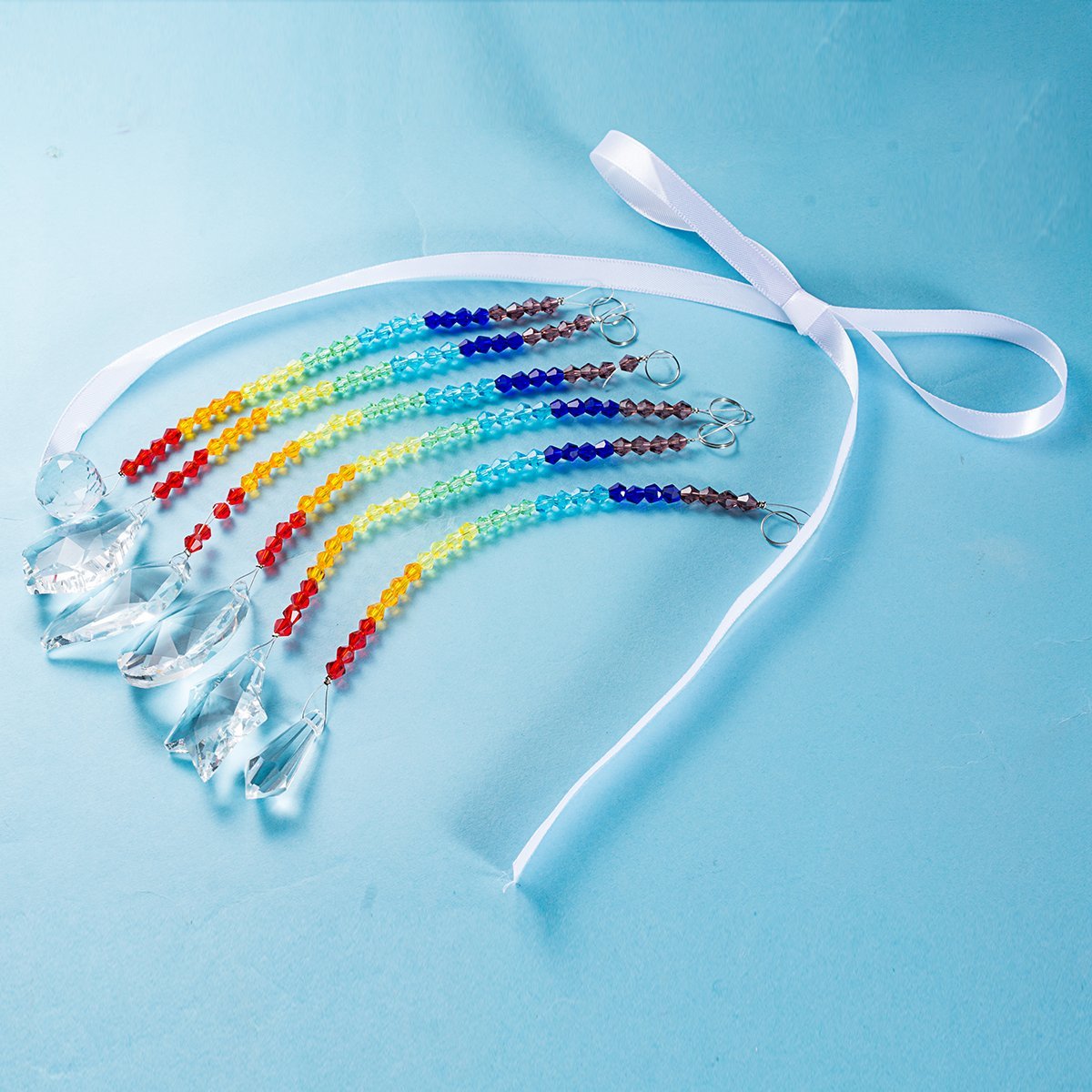 Rainbow crystal suncatcher strands with faceted glass pendants and a white ribbon tie on a blue background