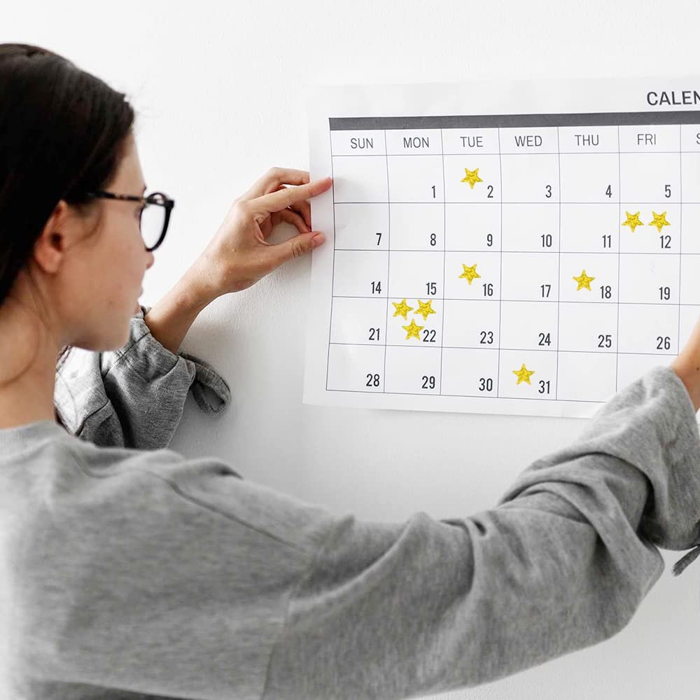 Woman placing holographic gold star stickers on a calendar grid, showing a lifestyle use case.