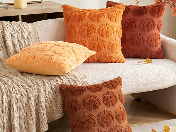 Four decorative throw pillows with embossed pumpkin designs on a sofa with a cable-knit throw blanket.