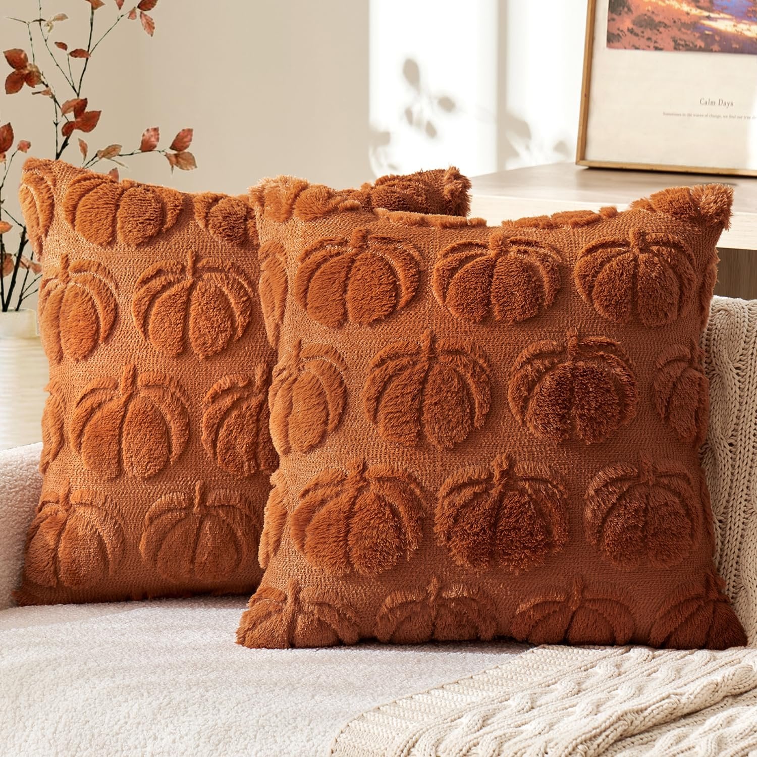 Two dark rust faux fur throw pillow covers with embossed pumpkins on a couch.