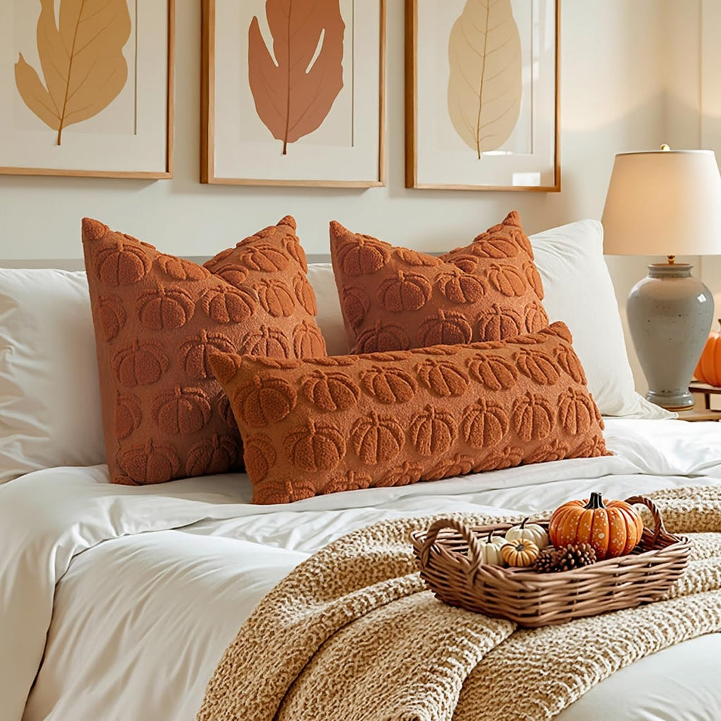 Set of two dark rust pumpkin textured throw pillow covers on a bed with a basket of pumpkins