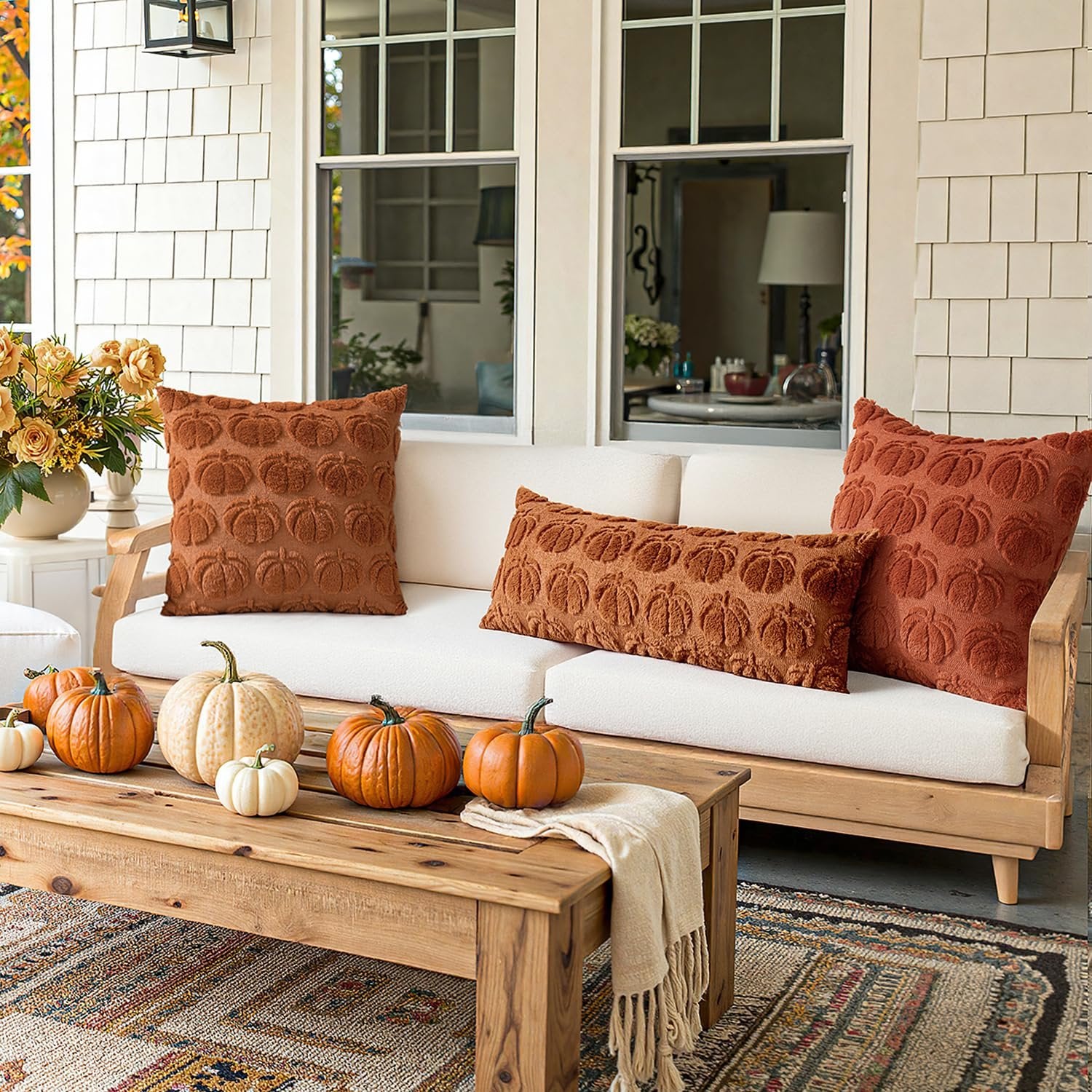 Set of two dark rust pumpkin throw pillow covers with textured pumpkin pattern on a couch with pumpkins on a coffee table.