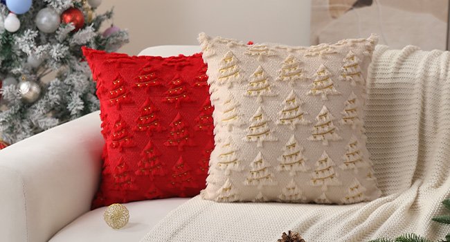 Two Christmas pillow covers, one red and one beige, with embroidered trees and gold lights, displayed on a sofa next to a decorated Christmas tree.