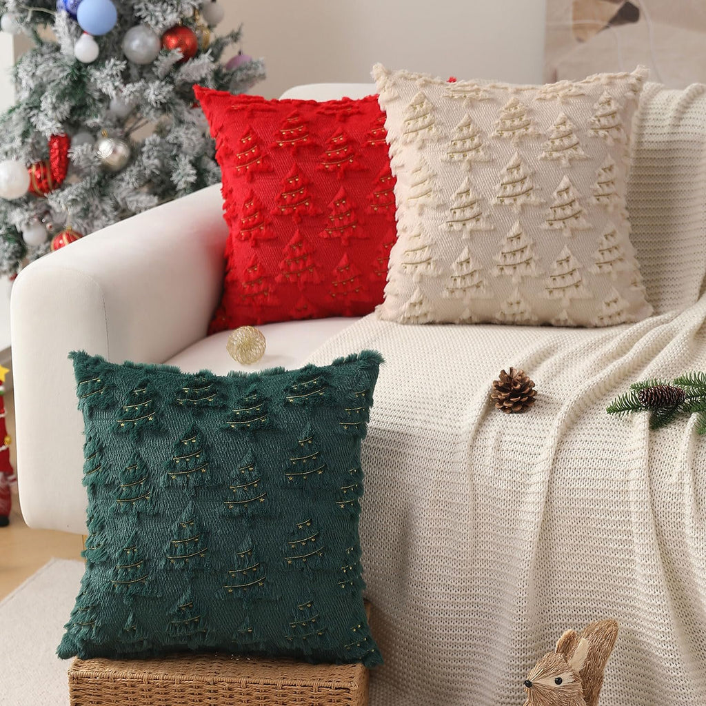 Three Christmas throw pillows with embroidered trees and lights on a sofa next to a decorated tree.