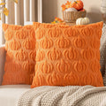 Two orange faux fur pumpkin-patterned throw pillow covers on a couch with a knit blanket.