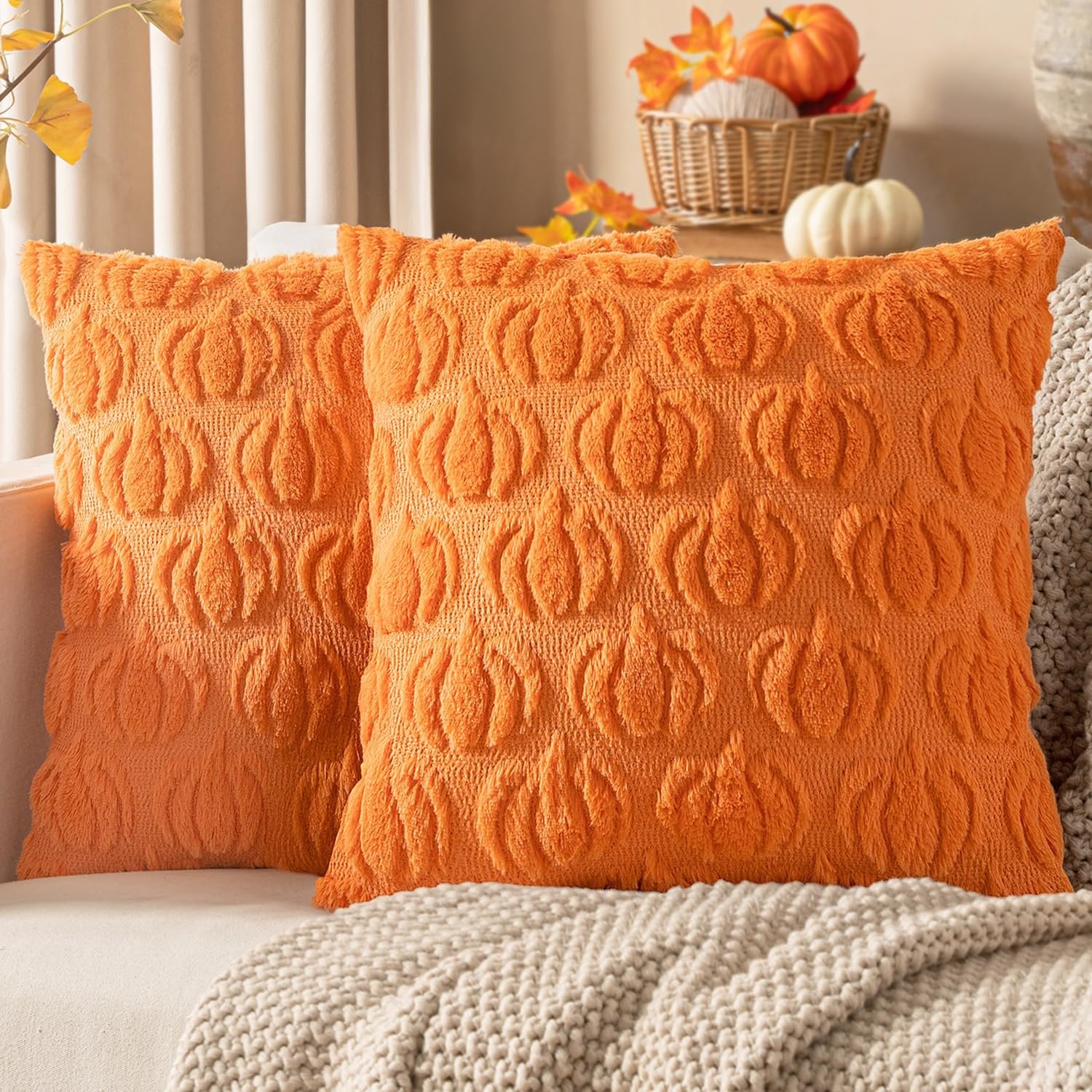Two orange faux fur pumpkin-patterned throw pillow covers on a couch with a knit blanket.