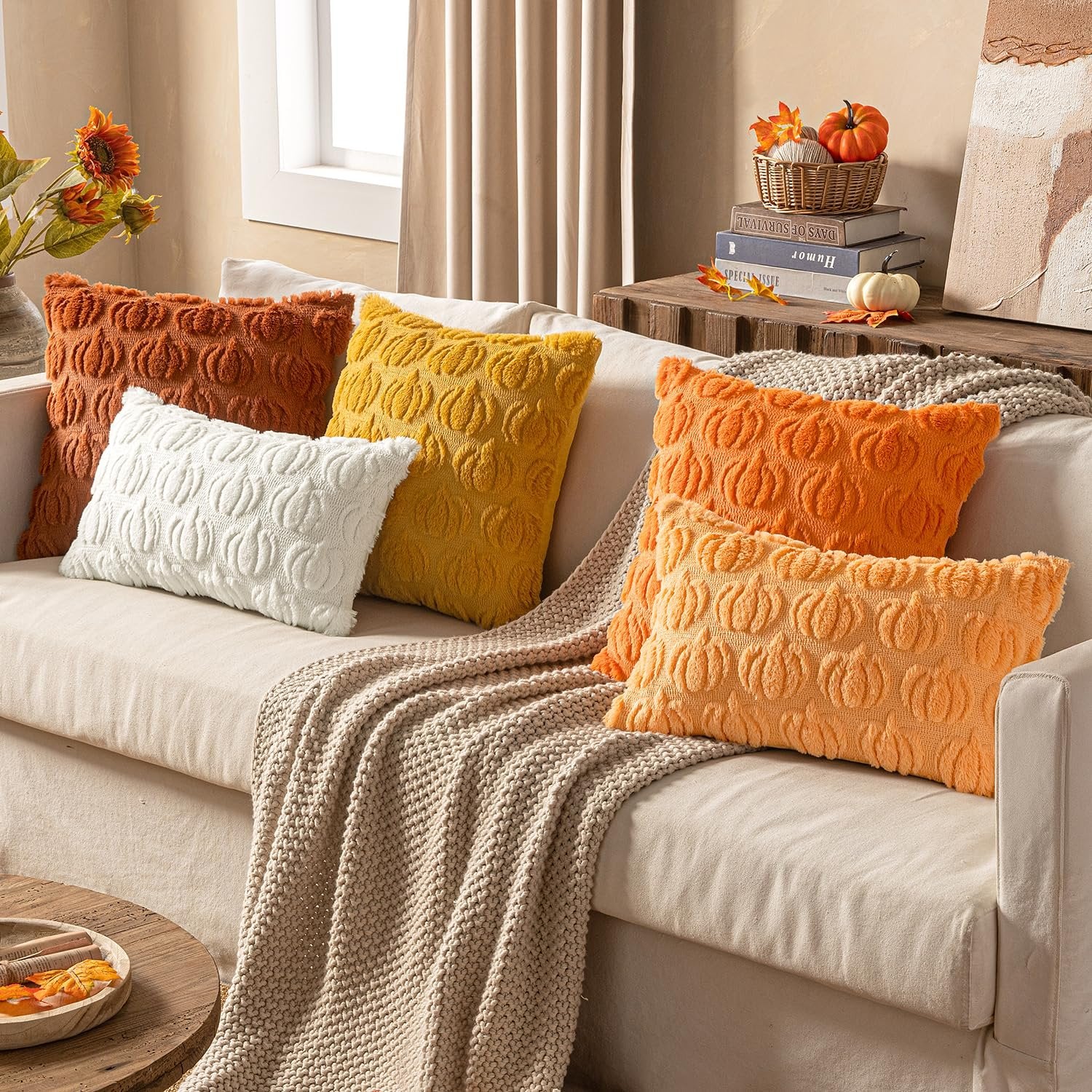 Set of six faux fur pumpkin-patterned throw pillow covers in orange, yellow, and white arranged on a sofa with a knit blanket.