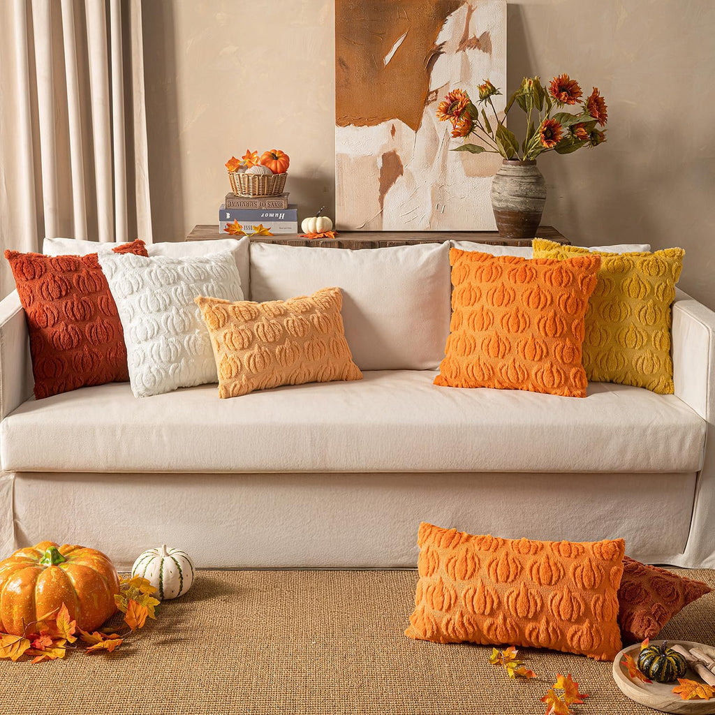 Several faux fur pumpkin-shaped throw pillows in various fall colors arranged on a sofa and floor, with decorative pumpkins and autumn leaves.