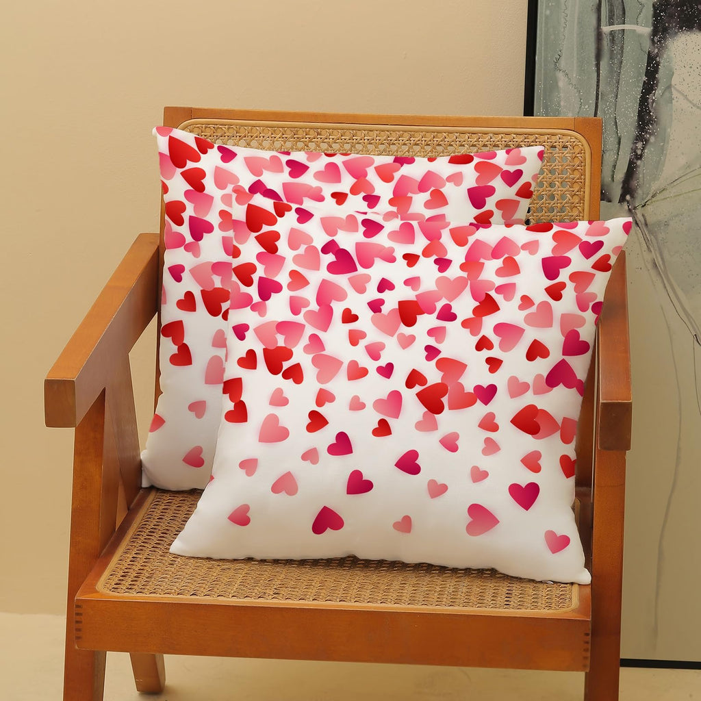 Two white pillow covers with a scattered pink and red heart pattern, displayed on a wooden chair.