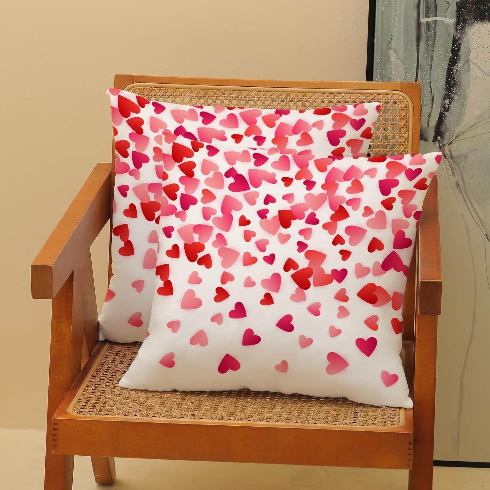 Two white pillow covers with a scattered pink and red heart pattern, displayed on a wooden chair.