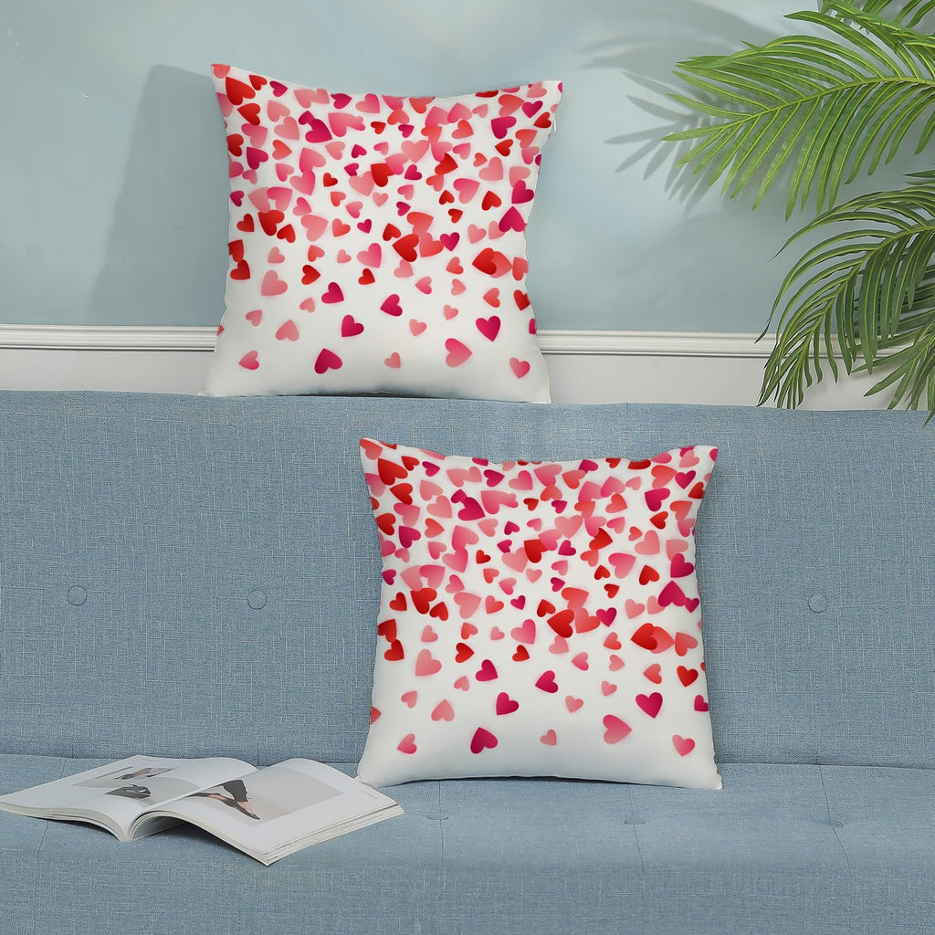 Two decorative throw pillows with a scattered pink and red heart pattern on a blue sofa.