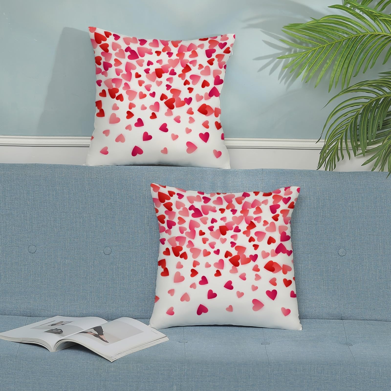 Two decorative throw pillows with a scattered pink and red heart pattern on a blue sofa.