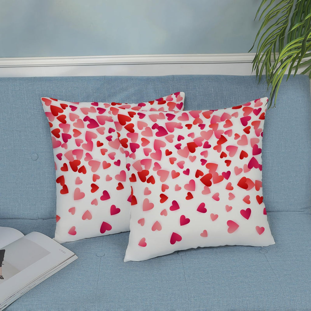 Two white throw pillow covers with scattered pink and red hearts, displayed on a blue sofa.