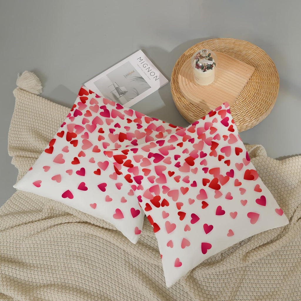 Two white pillow covers with a scattered pink and red heart pattern, laid on a cream blanket.