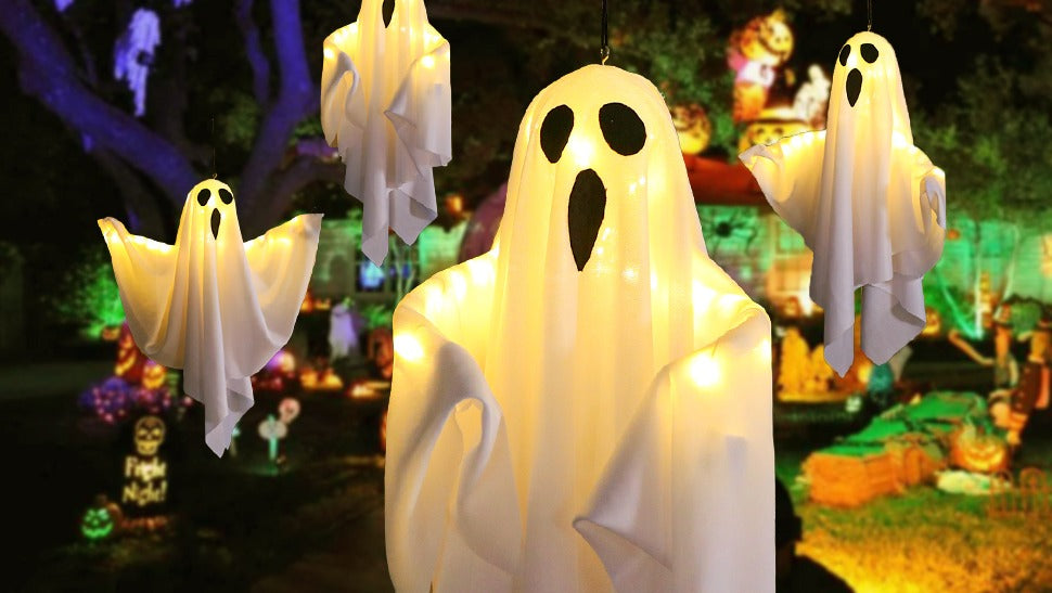 Several light-up hanging ghost decorations with warm white LEDs displayed outdoors at night.