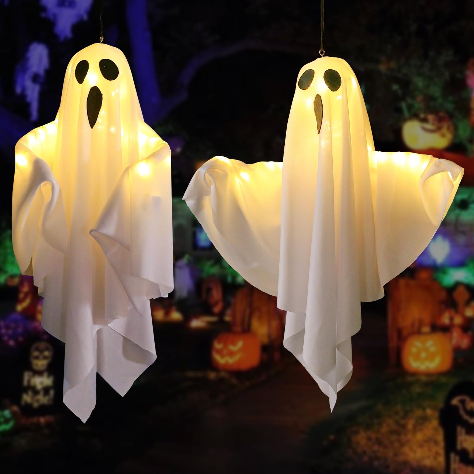 Two light-up hanging ghost decorations with warm white LEDs, displayed outdoors at night with Halloween decorations in the background.