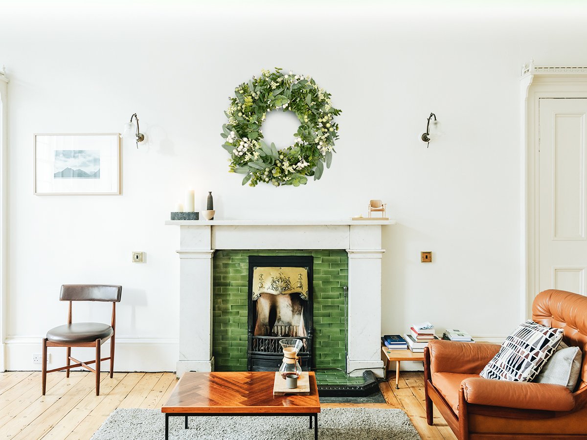 Green eucalyptus wreath with white berries hanging above a fireplace in a living room setting