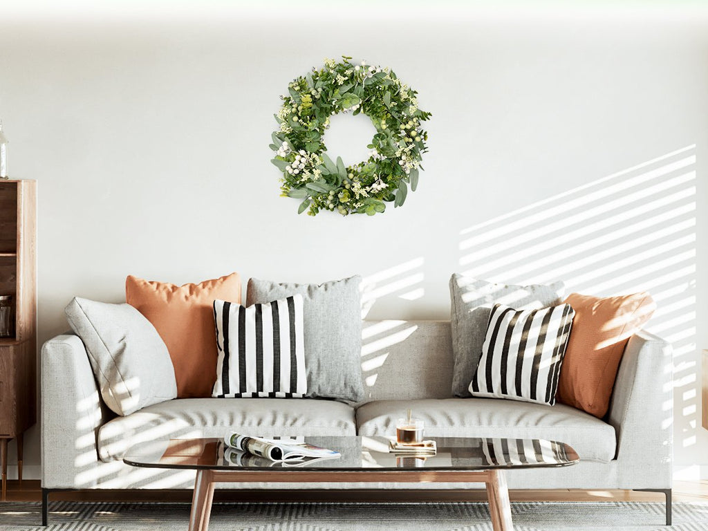 Green eucalyptus and white berry wreath hanging above a sofa with decorative pillows and a coffee table.