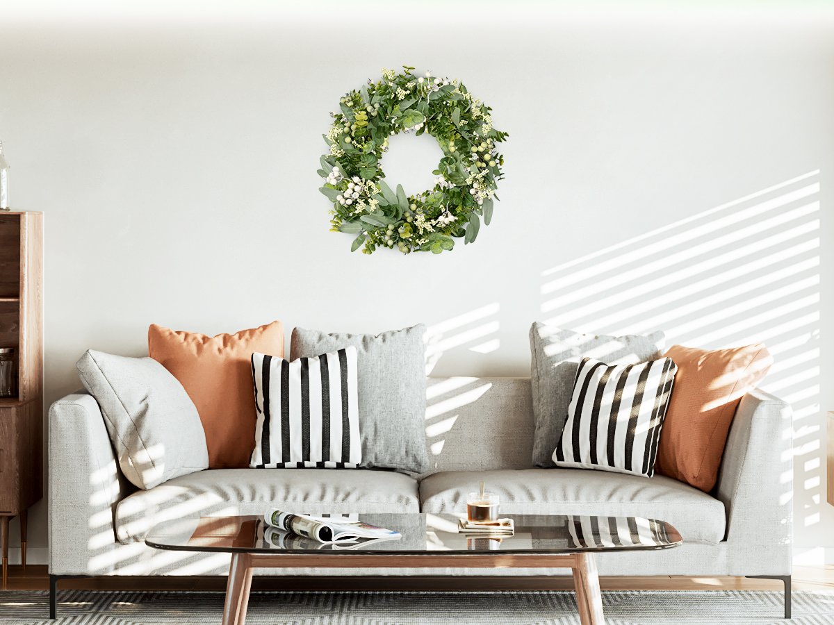 Green eucalyptus and white berry wreath hanging above a sofa with decorative pillows and a coffee table.