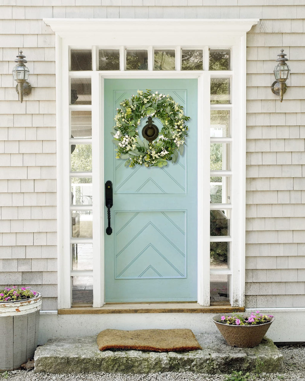 Green eucalyptus and white berry wreath hanging on a light blue front door with sidelights and a doormat.
