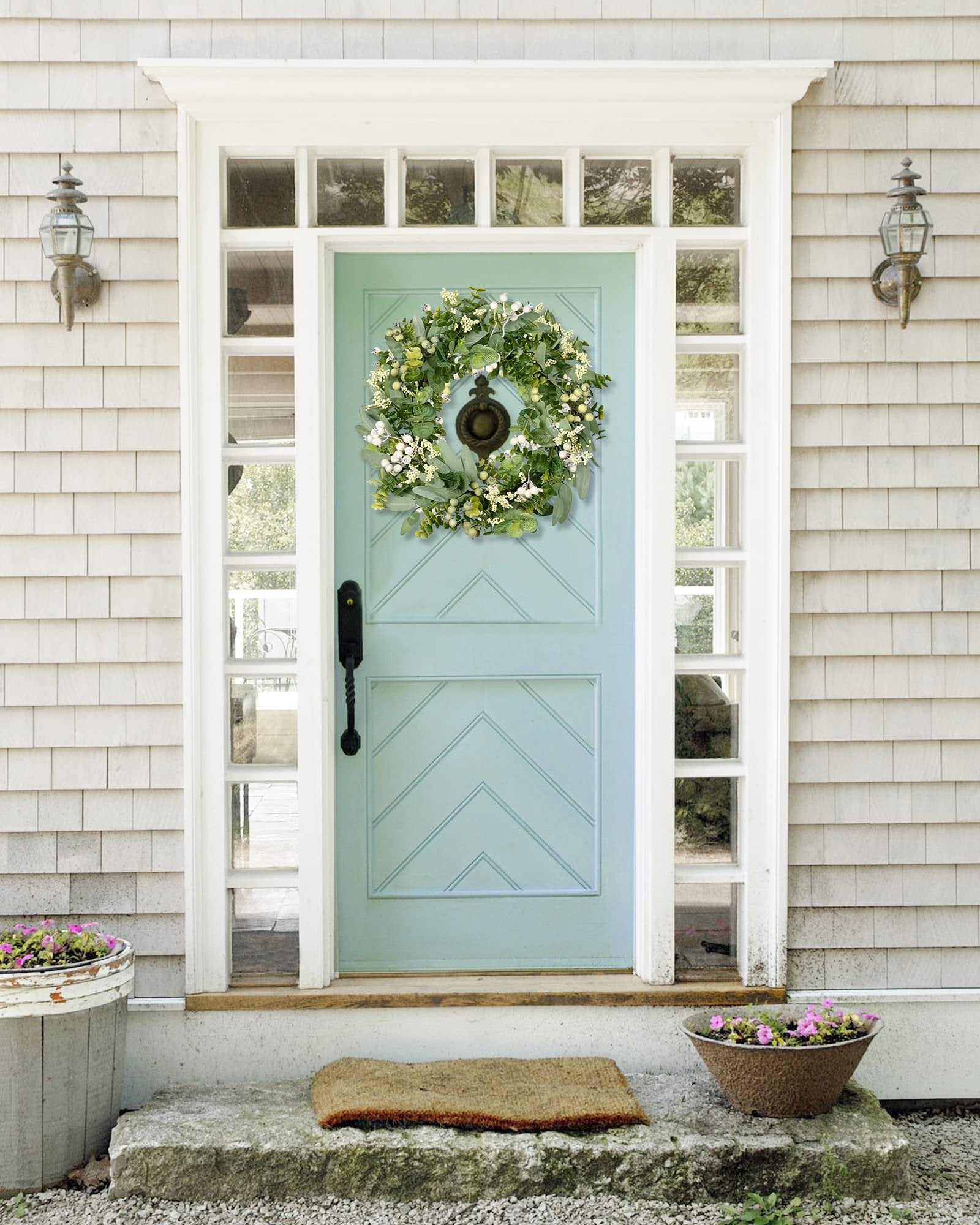 Green eucalyptus and white berry wreath hanging on a light blue front door with sidelights and a doormat.