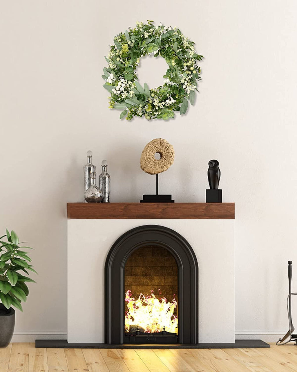 Green eucalyptus and white berry wreath hanging above a fireplace with a fire burning