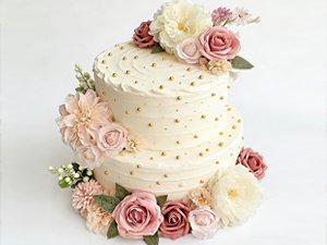 Two-tier frosted cake decorated with dusty blush pink artificial roses and gold beads