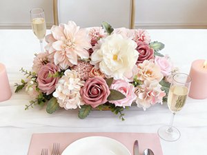 Dusty blush pink artificial rose bouquet centerpiece arrangement on a white tablecloth with champagne flutes and candles.