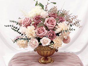 Dusty blush pink artificial rose bouquet arrangement in a gold urn vase, set on a pink cloth.