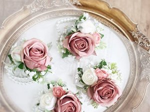 Dusty blush pink artificial rose bouquets with white accents and pearl strands arranged on a decorative tray.