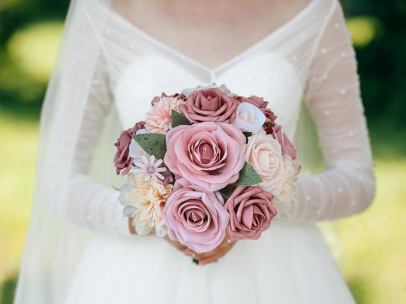 Bride holding a dusty blush pink artificial rose bouquet with a white wedding dress and veil