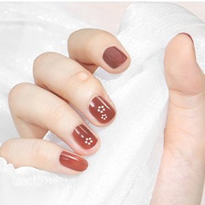 Close-up of a hand with short, brown-painted nails featuring small white floral designs.