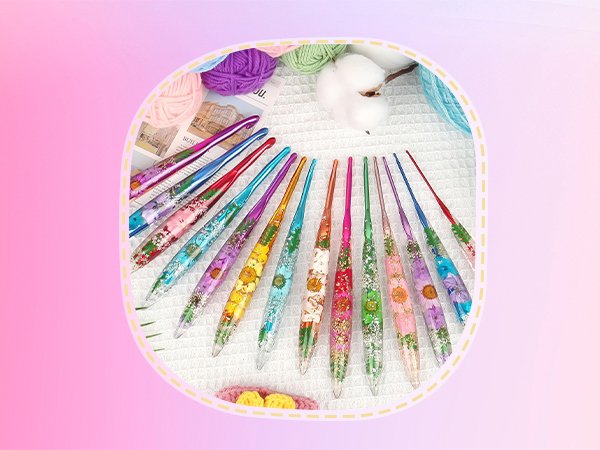 Set of colorful crochet hooks with dried flowers embedded in resin handles, surrounded by yarn and cotton balls.