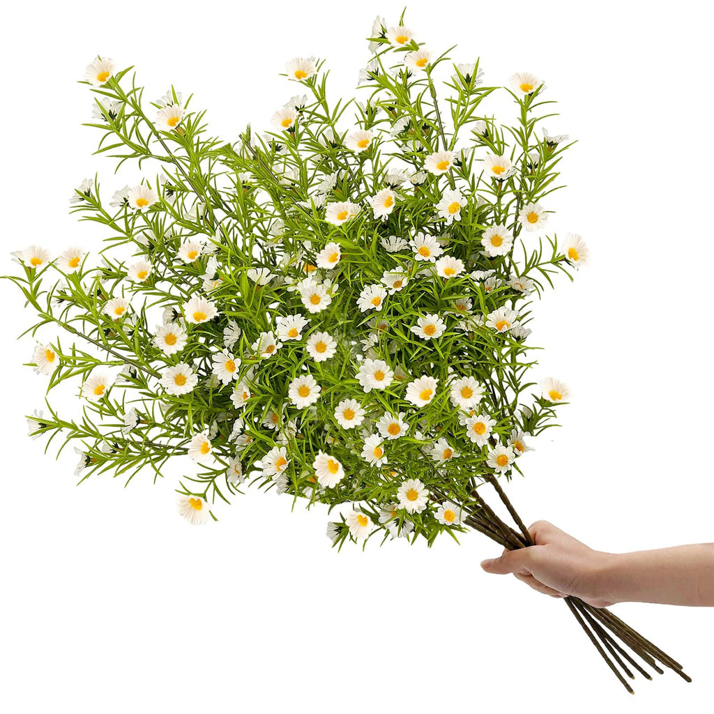 Hand holding a bouquet of artificial white daisies with green stems and leaves against a white background.