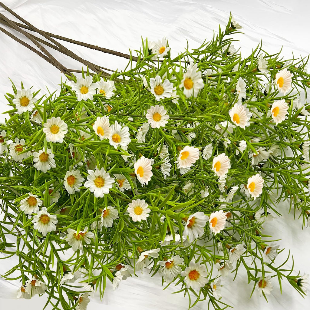 Bunch of artificial white daisy flowers with green foliage on a white textured background.