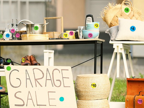 Garage sale setup with various items for sale, including kitchenware, shoes, and home decor, all marked with price stickers.