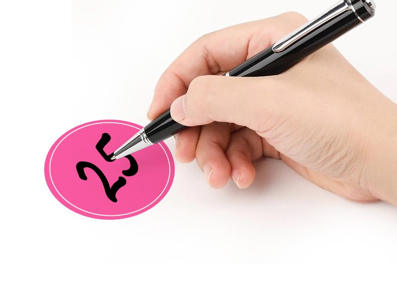 Hand holding a pen writing the number 25 on a pink oval sticker