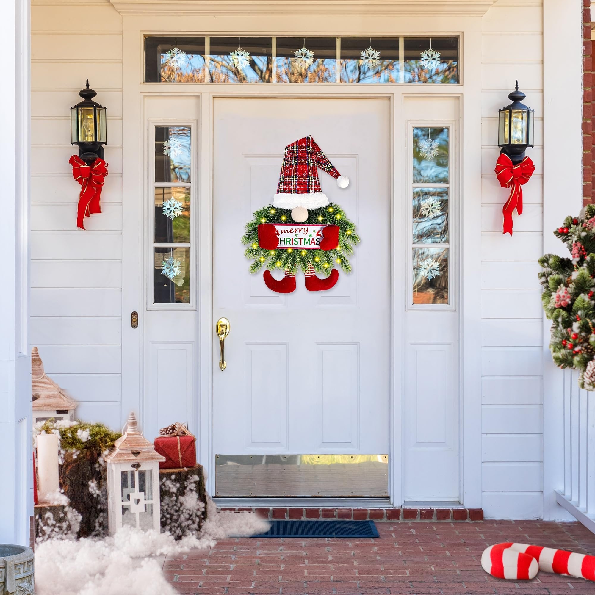 Christmas gnome wreath with lights and 'merry CHRISTMAS' sign hanging on a white door, decorated porch with lanterns and gifts