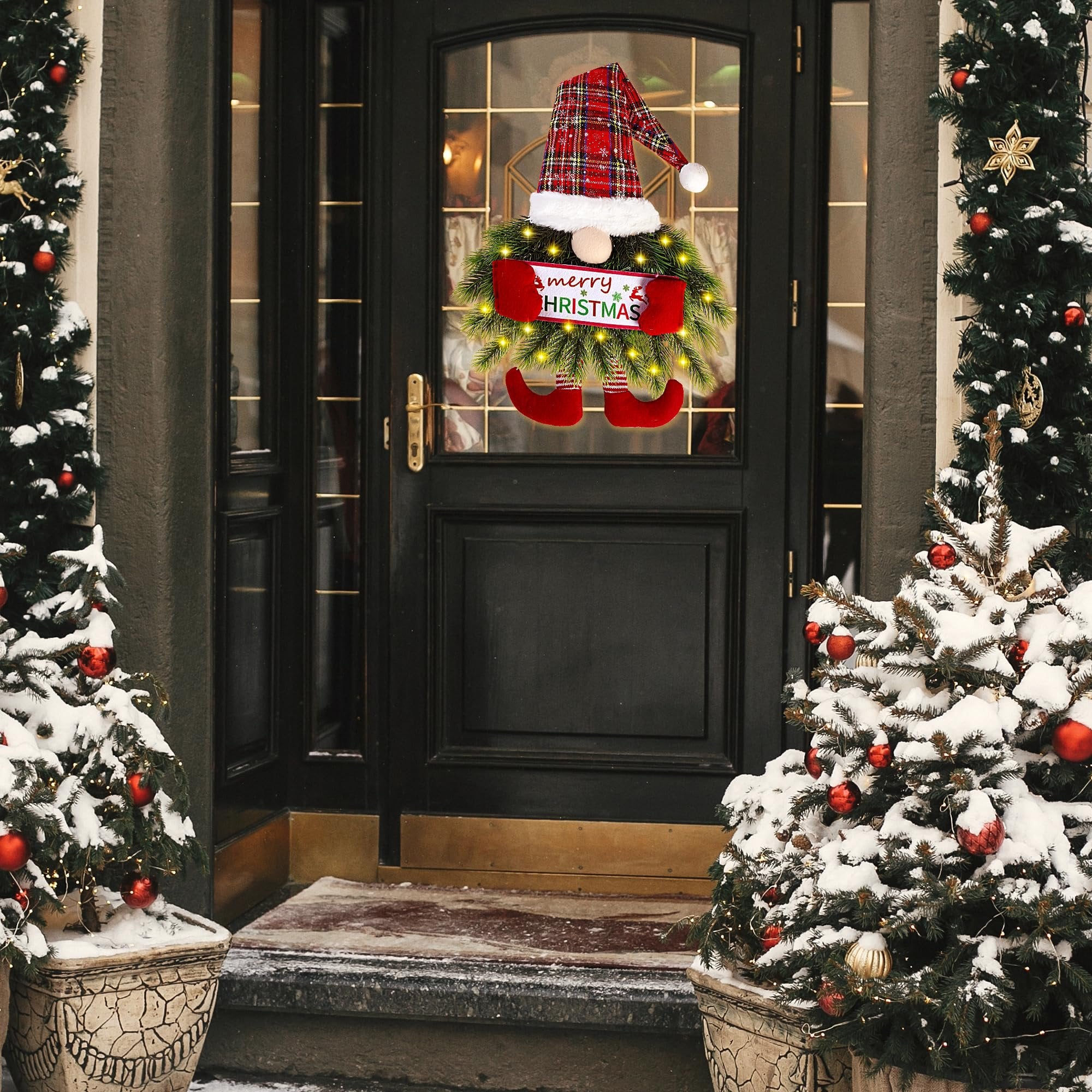 Christmas gnome wreath with plaid hat and red boots hanging on a front door, surrounded by snowy trees.