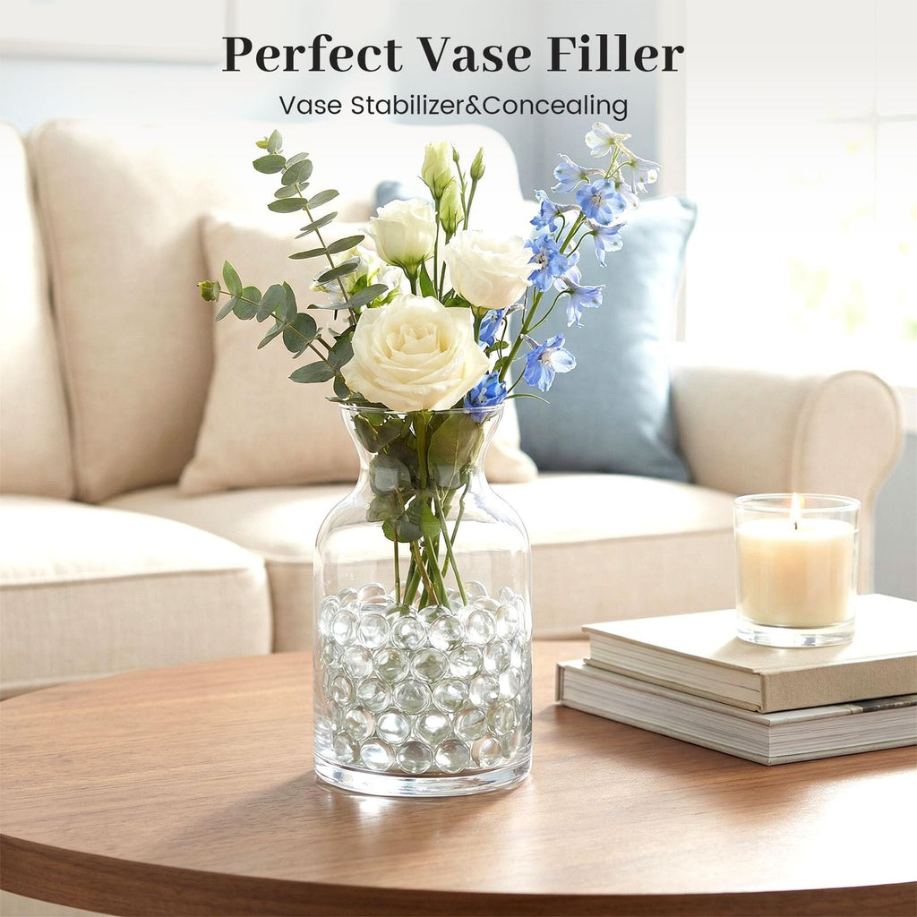 Clear flat glass marbles filling a vase with flowers and a lit candle on a table