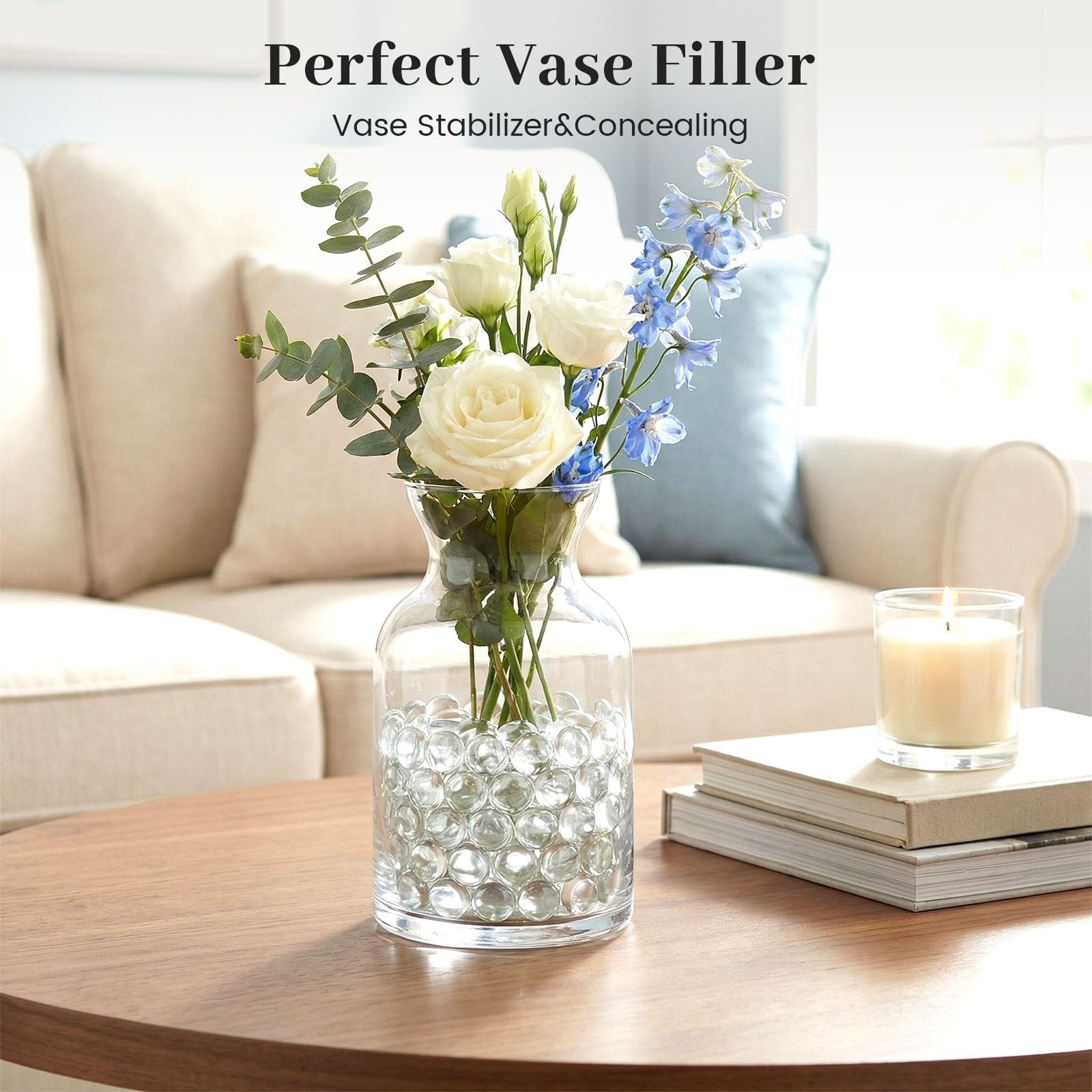 Clear flat glass marbles filling a vase with flowers and a lit candle on a table