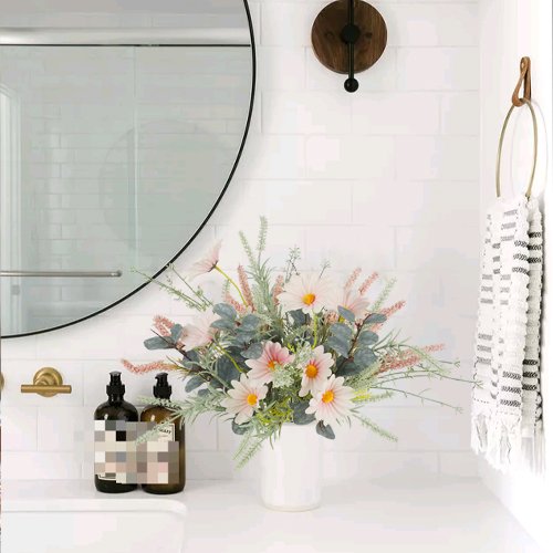Artificial wildflower bouquet with pink daisies and eucalyptus in a white vase on a bathroom counter.